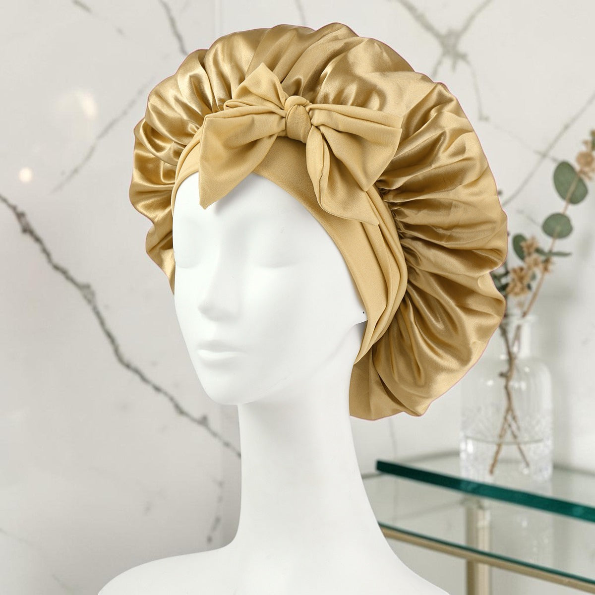Gorro de satén dorado PERENNE Silk Slumber de zafiropulse con lazo decorativo sobre maniquí blanco