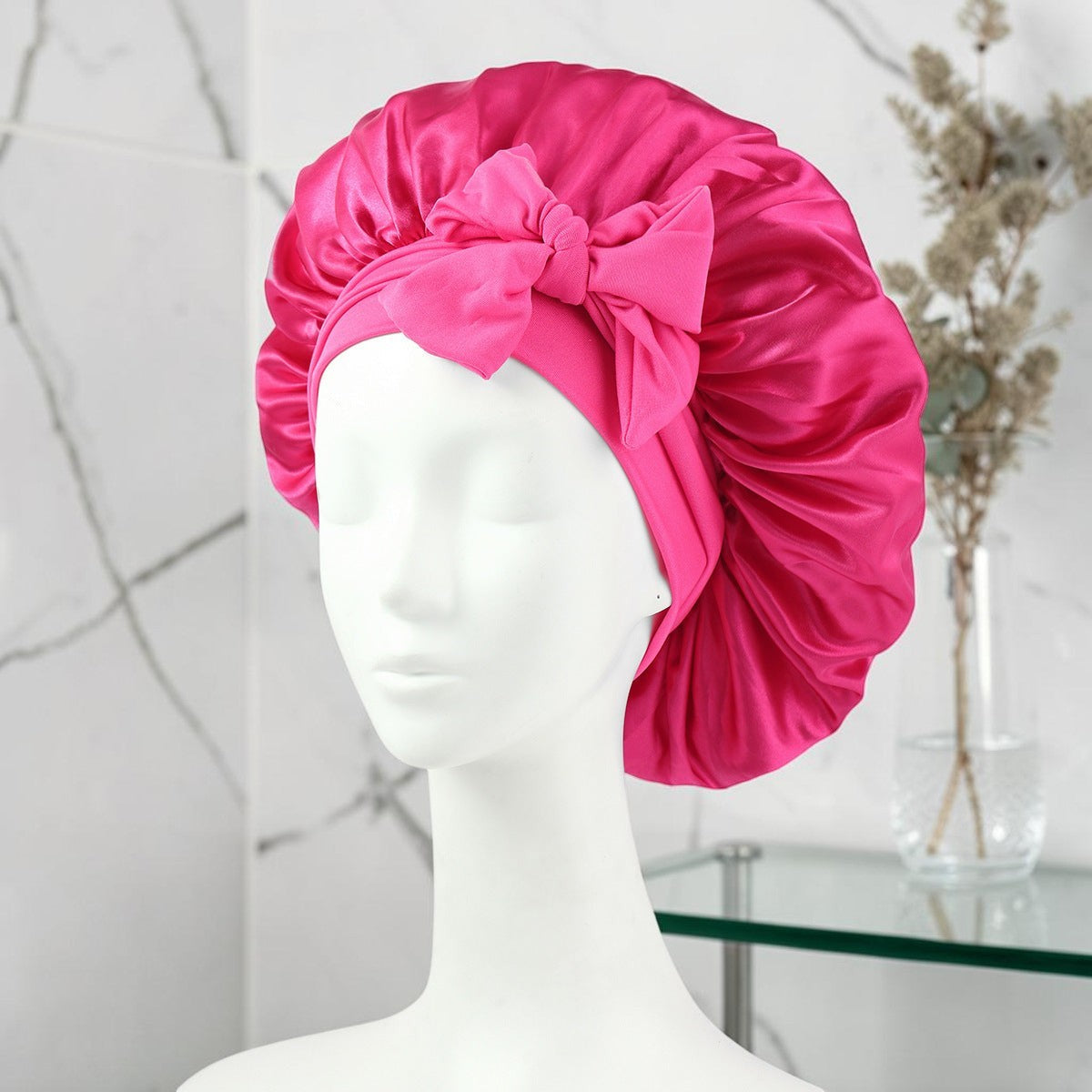 Gorro de satén fucsia PERENNE Silk Slumber de zafiropulse con lazo decorativo sobre maniquí para cuidado capilar