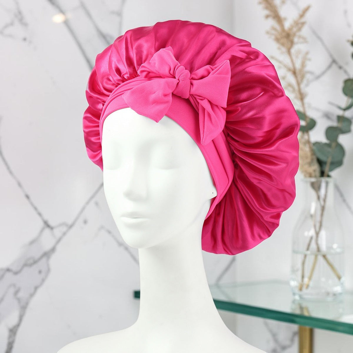 Gorro de satén fucsia PERENNE Silk Slumber de zafiropulse con lazo decorativo sobre maniquí para cuidado capilar