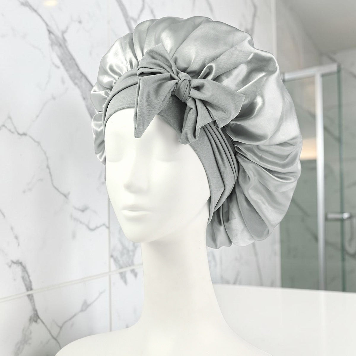 Gorro de satén plateado PERENNE Silk Slumber de zafiropulse con lazo decorativo sobre maniquí para cuidado capilar